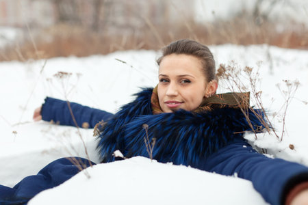 Happy girl in coat  lying down on the snow in winter
