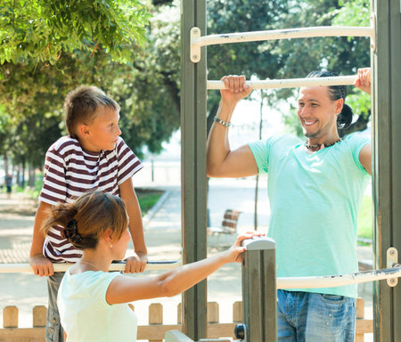 Happy parents with child  training with pull-up bar at playground 