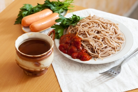 Supper. Buckwheat  spaghetti pasta with  ketchup and sausages in plates on tableの写真素材