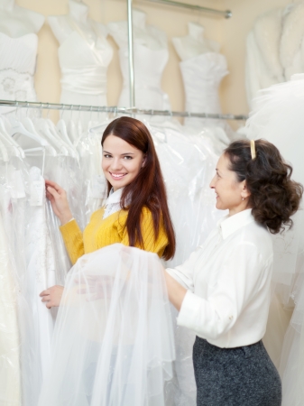 pretty bride chooses bridal outfit. Friendly shop consultant helps her. Focus on girlの写真素材