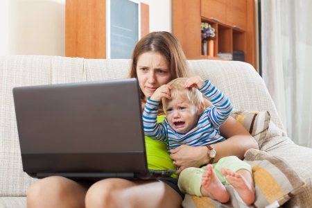 sorehead mother with crying baby working online with laptop at homeの写真素材
