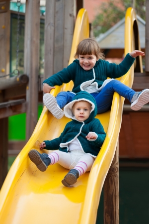 two happy children  on slide at playground in autumnの写真素材