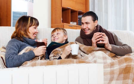Happy parents and teenage son with cups of tea warming near warm calorifer in homeの写真素材