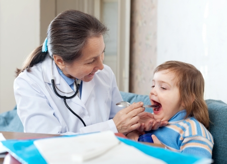 Doctor looks mouth of 2 years baby patient on couchの写真素材
