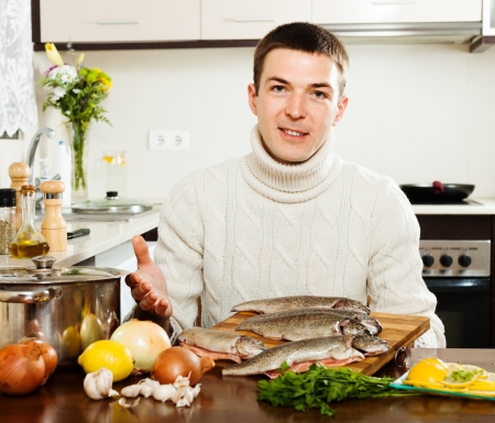 Handsome man with trout fish  in home kitchen の写真素材