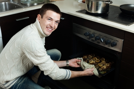 Happy handsome man takes the cooked fish on a baking sheet from the ovenの写真素材