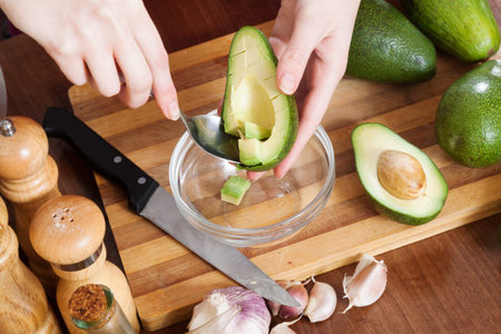 Closeup of female hands cooking with avocado at table in home kitchen