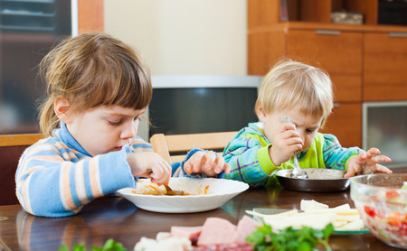 Baby girls eating at wooden table in home interiorの写真素材