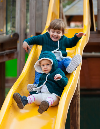 two happy children in jackets on slide at playground in autumnの写真素材