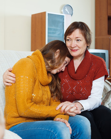 Mature mother comforting crying adult daughter in homeの写真素材
