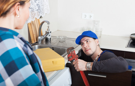 girl watching as worker repairing  water lines at home kitchenの写真素材