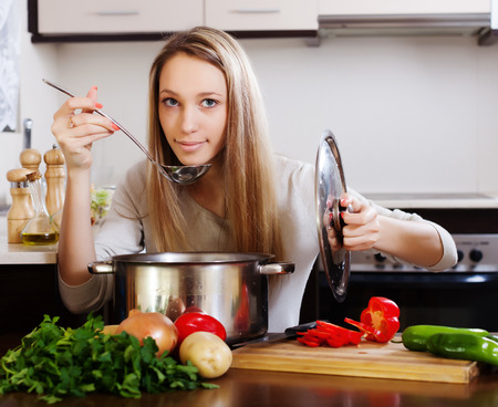 Ordinary blonde woman  with ladle cooking soupの写真素材