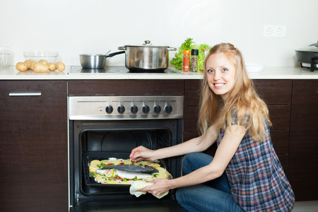 housewife cooking saltwater fish and potatoes on sheet pan in ovenの写真素材