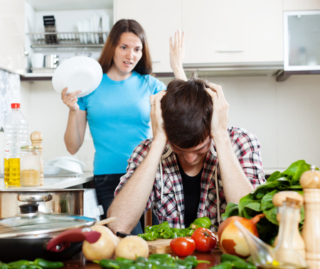 Sad man with angry wife at kitchen. Focus on guyの写真素材