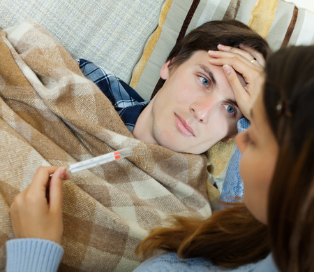 Woman caring for sick guy who high temperature in living room.の写真素材