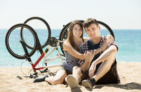 Smiling young couple with bicycles at sandy beachの写真素材