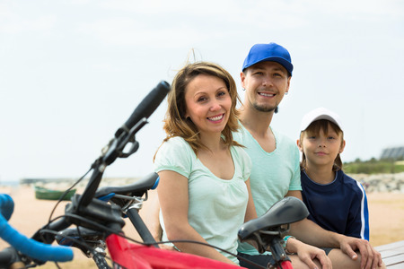 Positive parents and boy with bicycles at seashoreの写真素材