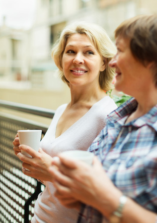 Two cheerful mature women drinking tea on balcony and smilingの写真素材