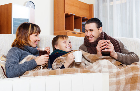 Happy parents and teenage son warming near warm heater in homeの写真素材