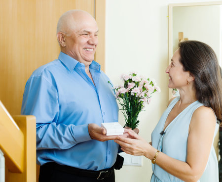 Smiling mature man giving jewel  to woman at home doorの写真素材
