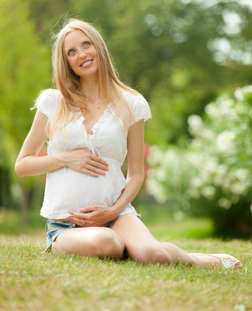 Happy pregnant woman relaxing on grass in  summer parkの写真素材