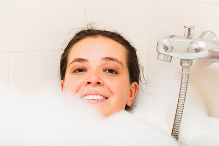 Smiling girl laying with foam in bathtubの写真素材