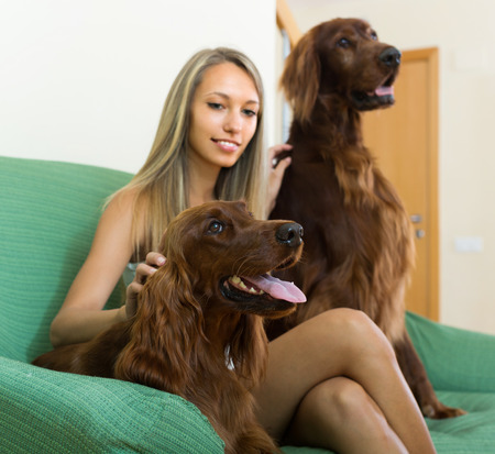 Attractive girl sitting on sofa with two Irish setters and smiling. Focus on dogの写真素材