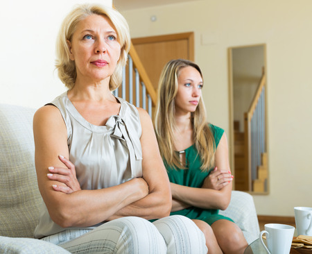 Upset mature woman and sad adult daughter having quarrel   in homeの写真素材