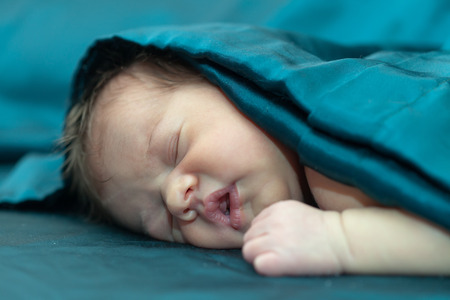 newborn baby sleeps under blanketの写真素材