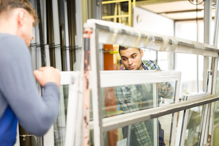 Two adults working in uniform examining a window at workshopの写真素材