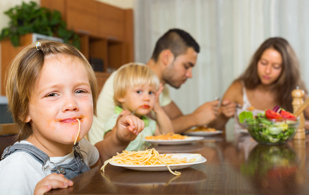 Smiling family with two little children eating with spaghetti at table. Focus on girlの写真素材