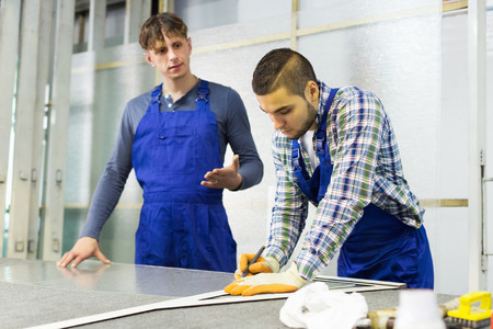 Two careful workmen cutting glass for windows at workshopの写真素材