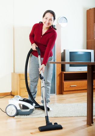 Happy mature woman with vacuum cleaner on parquetの写真素材