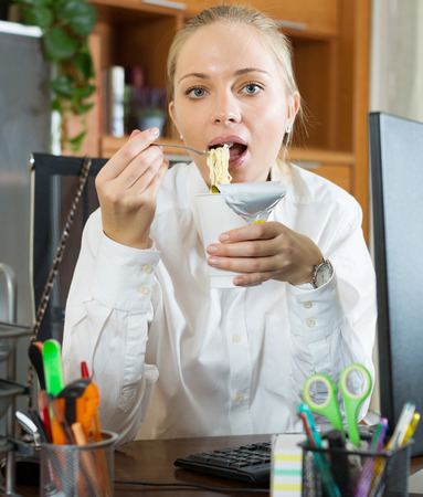 Hungry employee eating unhealthy noodles at officeの写真素材