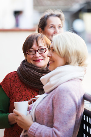Smiling pensioners in warm clothes having cup of hot tea on terraceの写真素材