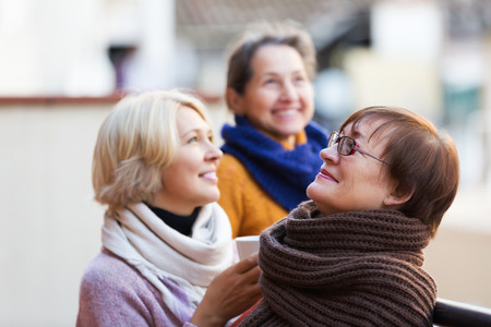 Senior women in warm clothes having cup of hot tea on terraceの写真素材