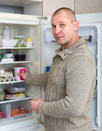 Adult male in the kitchen taking something from fridge to eatの写真素材
