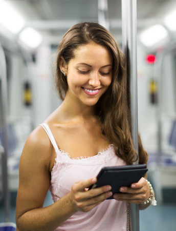 Smiling young woman using eBook in subway train at metroの写真素材