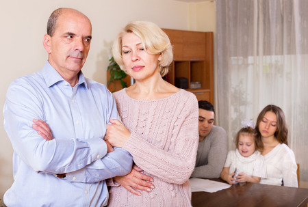Sad mature couple on   background of young parents with child   at homeの写真素材