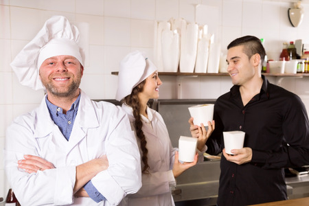 Portrait happy cook and client buying take-away food at eating houseの写真素材