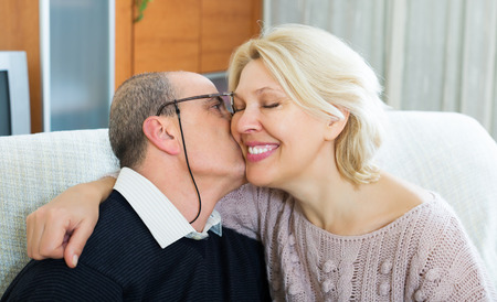 Portrait of loving smiling mature spouses sitting on sofa indoorの写真素材