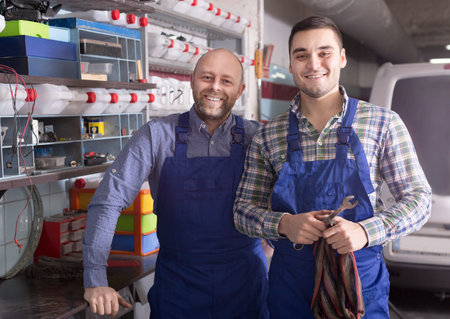 Two workmen standing near storage shelves at the auto repair shop