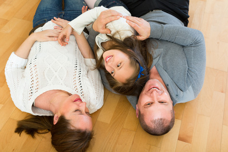 Happy smiling little girl with cheerful parents posing at floor at homeの写真素材