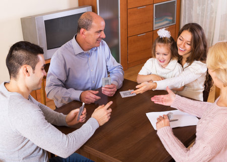 Portrait of smiling parents and their children playing cards together and keeping score indoor