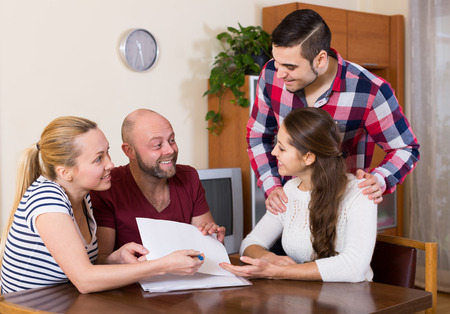 Young happy spouses sitting with documents and asking friends for adviceの写真素材