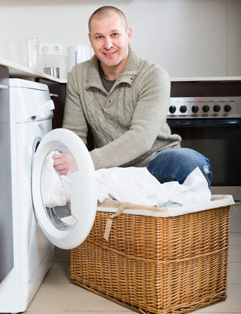 Home laundry. Happy smiling man using washing machine in kitchen at homeの写真素材