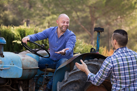 Two happy farmers talking near agricultural machinery at the shedの写真素材