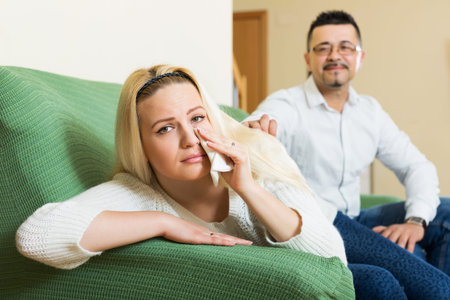 Man asking for forgiveness from sad girl after quarrel at home. Focus on girl