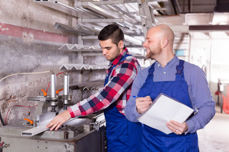 Two workers in coverall working with glass in factory