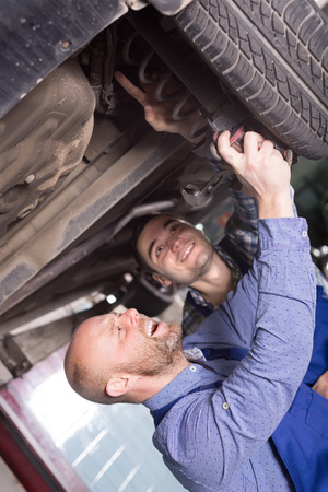 Two smiling car mechanics checking up pressure in tires at workshopの写真素材
